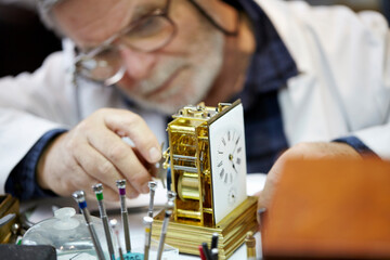 Mature Watchmaker repairing vintage pocket watch and clock on the workbench.  