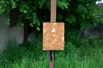 A rusty box on a pole. The box is suspended in the village. Old electrical panel.