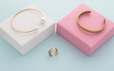 Modern golden bracelets on pink and white boxes and double shape ring on blue background