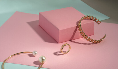 Chain shape golden bracelet and ring on pink box on green paper background with copy space