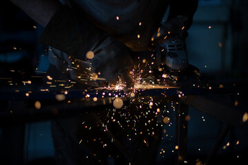 Work grinding machine. Sparks from the force of friction. A man in a workshop processes metal.