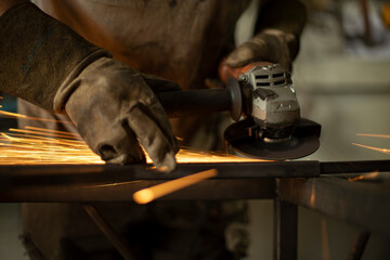 Metal processing with a grinder. Sparks from the tool. A man in the workshop wearing gloves with a grinder in his hand.