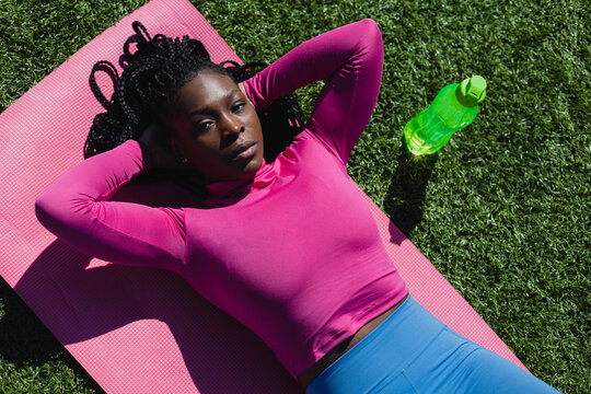 Tired black sportswoman relaxing on mat during training