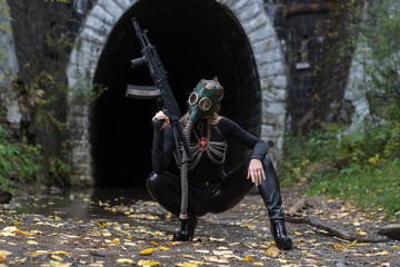 A woman in a black suit and gas mask with a machine gun in her hands