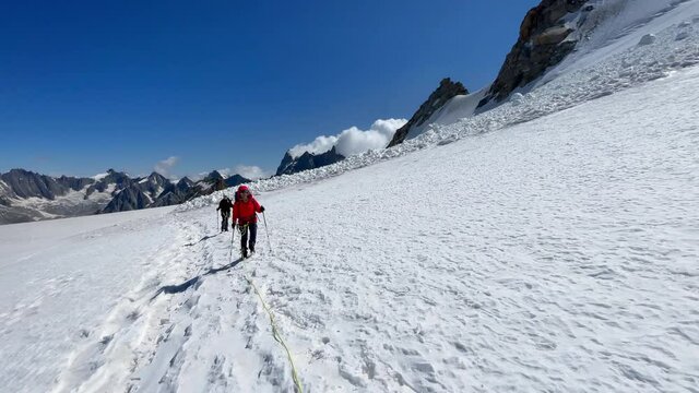 Two young women Rope team crossing the glacier dressed mountaineering clothes with ice axes walking by snowy slopes. People extreme activities sporty concept 4K handheld video.