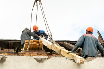 Two workers are repairing the roof of an old building. Repair of the roof, replacement of ceilings and wooden beams, installation of new red tiles.