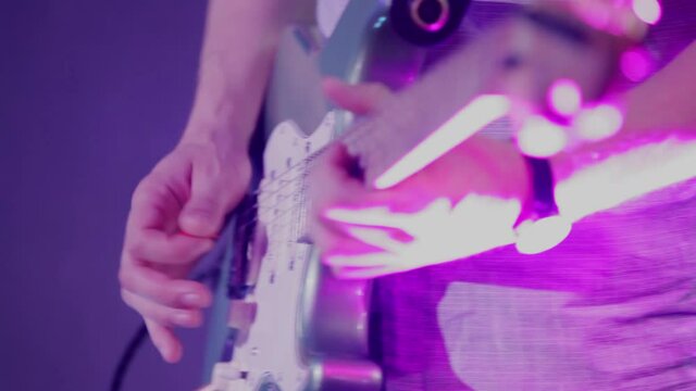 A white-skinned male musician plays the electric guitar on stage at a concert or Christian worship service. Club spotlights in pink and blue shimmer as the guitarist plays chords