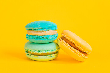 Sweet almond colorful unicorn blue yellow macaron or macaroon dessert cake isolated on trendy yellow modern fashion background. French sweet cookie. Minimal food bakery concept Copy space