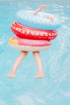 Kid in Stack of Inflatable Pool Tubes in Swimming Pool