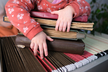 small child, baby, girl hold a stack of old photo albums on an archival metal cabinet with thin...