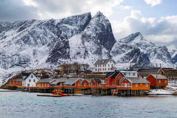 Lofoten islands, Norway, fishing village with red rorbu huts on the coast, snowy mountains in the background.