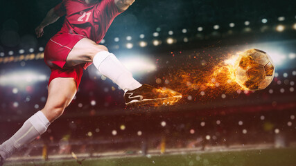 Close up of a soccer scene at night match with player in a red uniform kicking a fiery ball with...