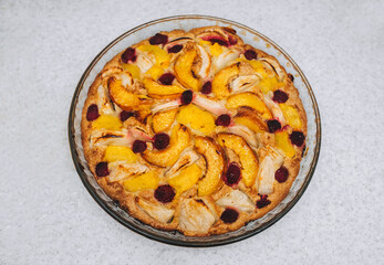 Delicious, fresh, baked pie made of apples, piers, raspberries close-up in a round glass form stands on a white table. Photography, concept.