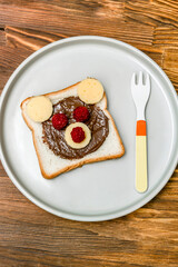 Funny bear face sandwich toast bread with peanut butter, cheese and raspberry on plate wooden background. Kids child sweet dessert breakfast lunch food close up