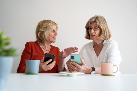 Senior friends at home looking at phone and talking
