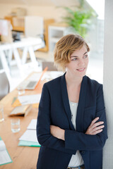 Portrait of woman leaning on column in office and smiling