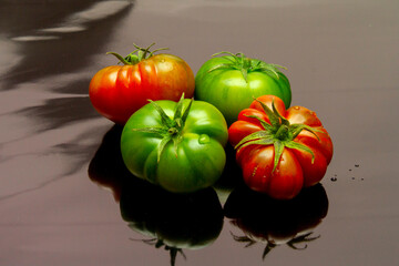 ripe and green raf tomatoes on reflective black surface - obrazy, fototapety, plakaty