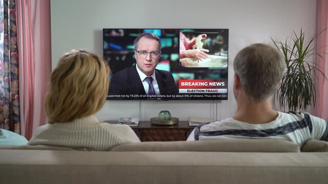 Family Couple Watching TV News Sitting on Couch in Living Room Together. TV Presenter Telling Breaking News about Politics, Elections and Voting Violations