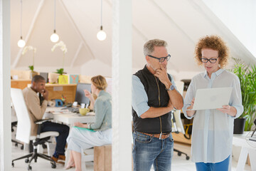 Naklejka premium Man and woman talking in office holding laptop