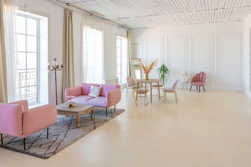 delicate and cozy light interior of the living room with modern stylish furniture of pastel pink color and white walls with stucco moldings in daylight