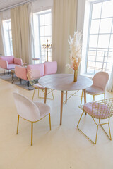 delicate and cozy light interior of the living room with modern stylish furniture of pastel pink color and white walls with stucco moldings in daylight