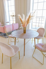delicate and cozy light interior of the living room with modern stylish furniture of pastel pink color and white walls with stucco moldings in daylight