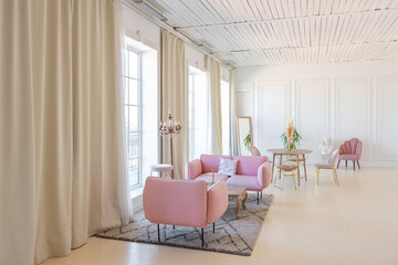 delicate and cozy light interior of the living room with modern stylish furniture of pastel pink color and white walls with stucco moldings in daylight