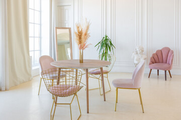 delicate and cozy light interior of the living room with modern stylish furniture of pastel pink color and white walls with stucco moldings in daylight
