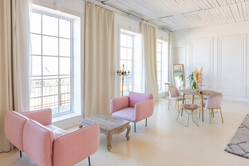 Fototapeta na wymiar delicate and cozy light interior of the living room with modern stylish furniture of pastel pink color and white walls with stucco moldings in daylight