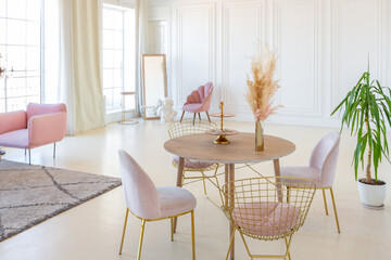 delicate and cozy light interior of the living room with modern stylish furniture of pastel pink color and white walls with stucco moldings in daylight