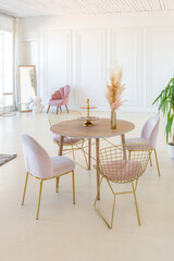 delicate and cozy light interior of the living room with modern stylish furniture of pastel pink color and white walls with stucco moldings in daylight