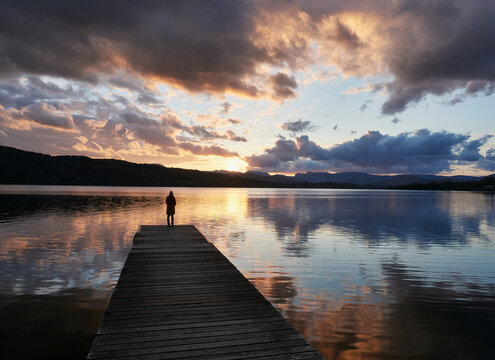 Female on a jetty watching the sunset over Lake Windermere. Lake District, UK.