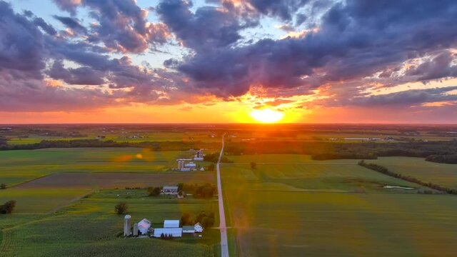 Colorful sunset sky over country road through farms and corn fields
