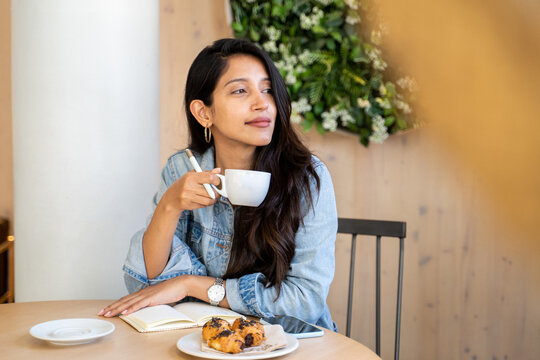 Young woman holding coffe cup looking away in cafeeria