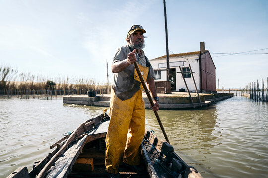 Fisherman standing in a boat using a wooden push pole to propel himself