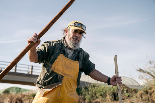 Low angle view of a fisherman standing in a boat holding two wooden pole