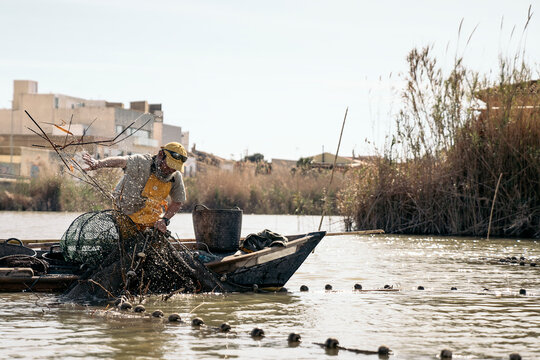 Fisherman in boat pulling net out of water with trapped fish