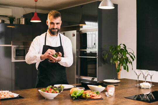 Positive chef preparing fresh herbs for dish 