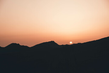 Siluetas de montañas y sol de atardecer.
