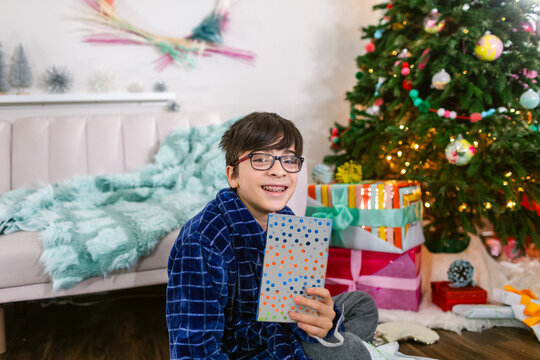 Happy boy with braces showing excitement a book by Christmas tree