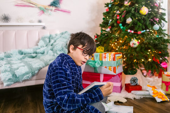 Boy reading book near Christmas tree