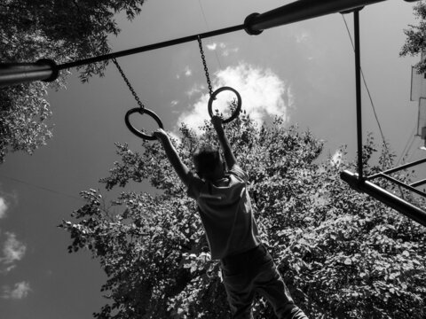 The boy is hanging on the rings.