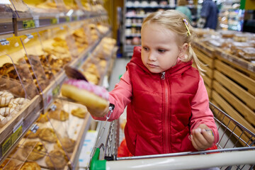 Little girl chooses pastries in the supermarket.