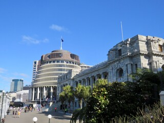 Photo of the Beehive and New Zealand Parliament Building, as people move about on the forecourt in front - obrazy, fototapety, plakaty