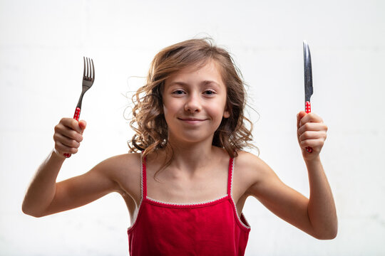 Playful young girl holding up a knife and fork