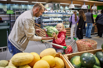 Father and little daughter are choosing watermelon in supermarket.