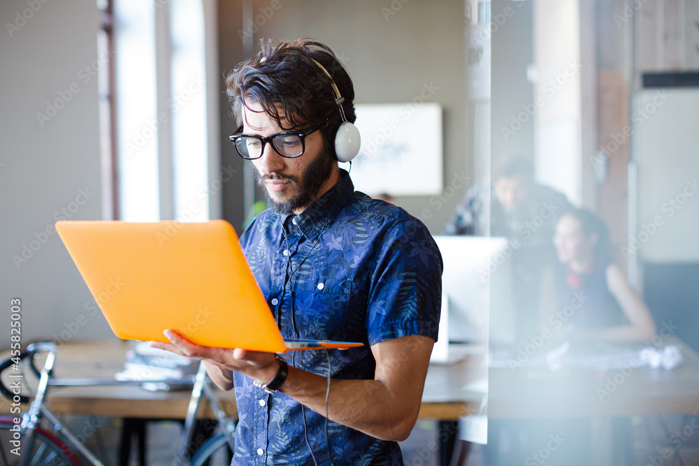 Wall mural Casual businessman wearing headphones and using laptop in office