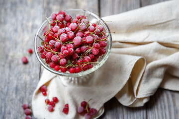 Frozen red currants in a glass vase on a cloth on a rustic wooden table. Close-up.