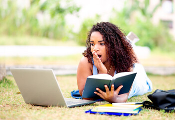 Student studying on college campus, with books and a Laptop. Young woman with surprised expression when seeing something on the computer.