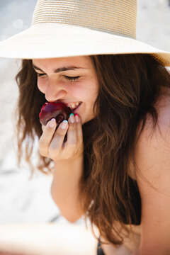 Happy woman eating plum on the beach